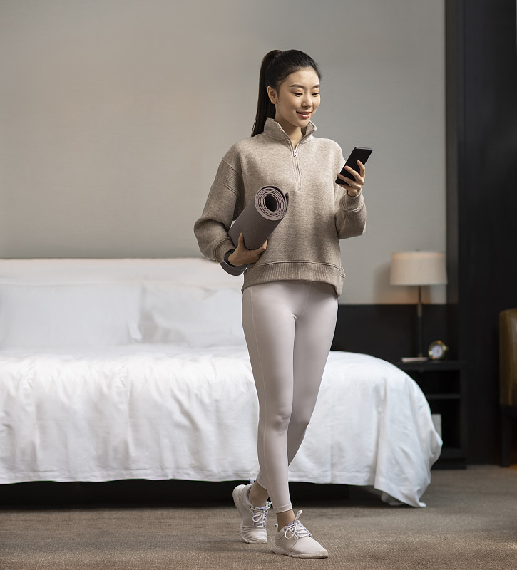 年轻女子拿着瑜伽垫和手机图片下载