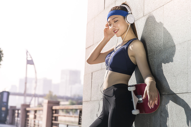 玩滑板的年轻女士运动后休息听音乐图片下载
